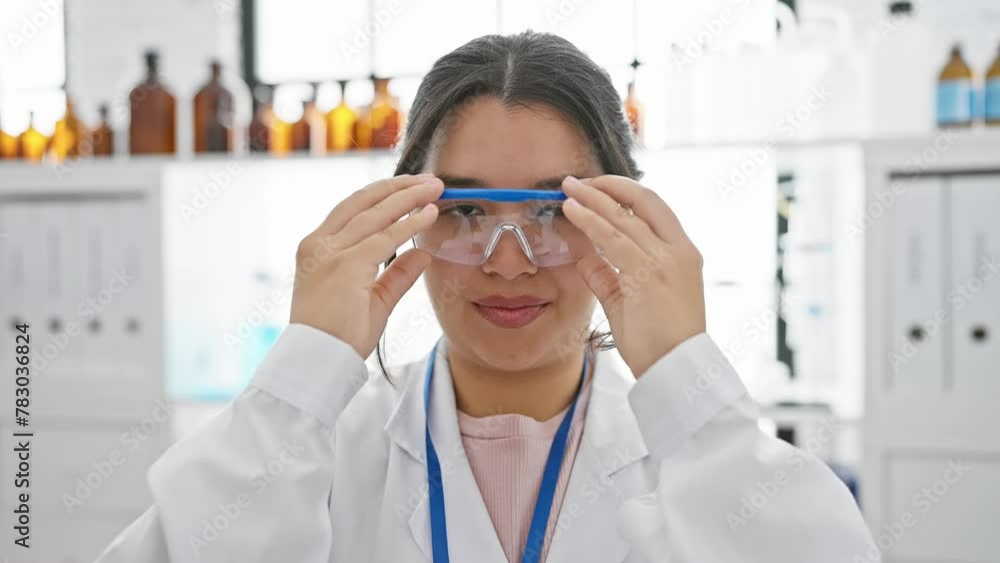 Confident hispanic woman in lab coat and safety glasses stands in a laboratory setting, portraying healthcare professionalism. Confident hispanic woman in lab coat and safety glasses stands in a laboratory setting, portraying healthcare professionalism.