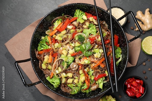 Wok with noodles, mushrooms, vegetables and other products on black table, flat lay