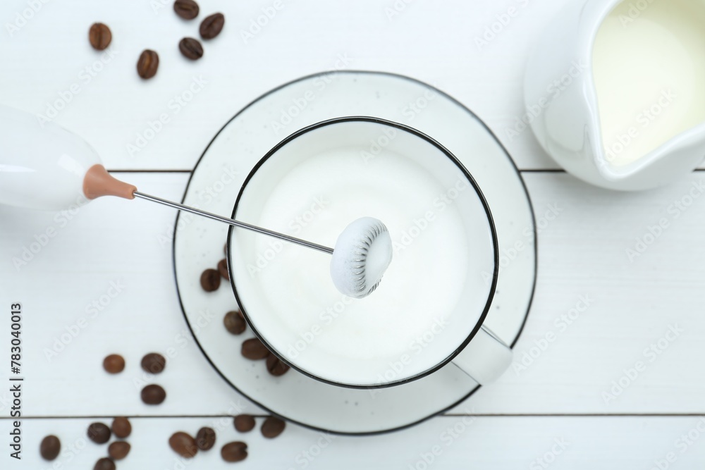 Flat lay composition with mini mixer (milk frother), whipped milk and coffee beans on white wooden table Flat lay composition with mini mixer (milk frother), whipped milk and coffee beans on white wooden table