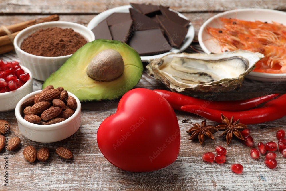 Natural aphrodisiac. Different food products and heart model on wooden table, closeup