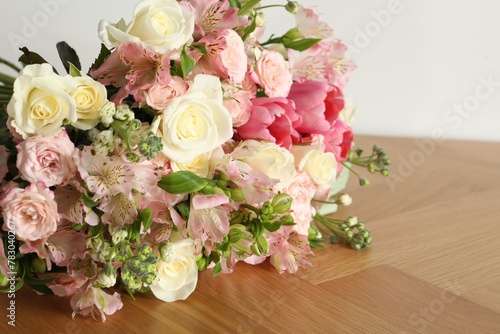 Beautiful bouquet of fresh flowers on wooden table near white wall  closeup. Space for text