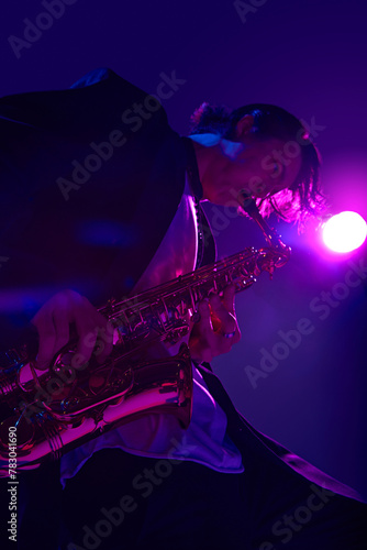 View from below of young talented man playing sax in vibrant pink neon light against dark studio background. Concept of music and art, hobby, concerts and festivals, modern culture. Ad