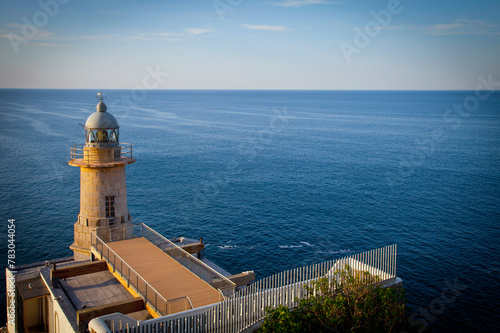 This vibrant image captures a coastal lighthouse standing tall at the edge of a cliff, overlooking the vast sea under clear skies photo