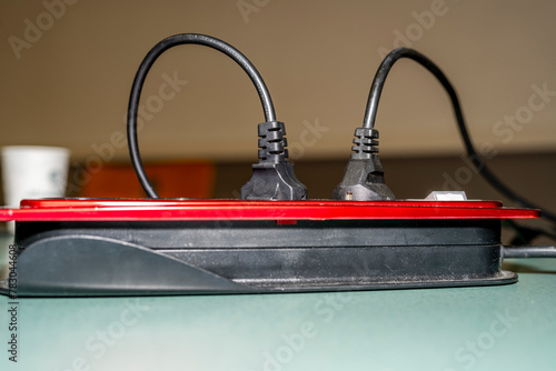 multiprise électrique rouge et noire avec deux prises branchées posé sur une table photo