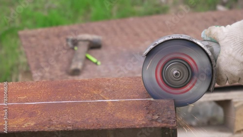 An angle grinder cuts old rusty metal, the worker's hands are gloved.