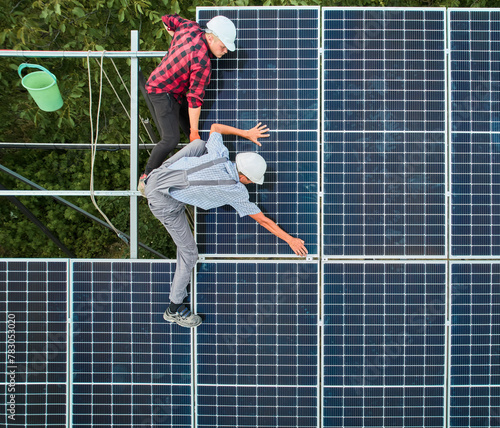 Aerial view of men technicians installing photovoltaic solar panels to high steel platform. Concept of alternative energy.