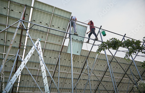 Male workers building photovoltaic solar panel system outdoors. Men electricians lifting solar module on metal rails. Renewable and ecological energy.