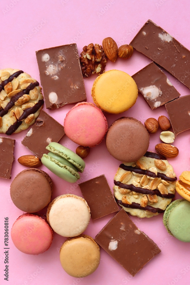 Pastel macarons, almond chocolate, peanut butter cookies and various nuts on bright pink background. Top view.