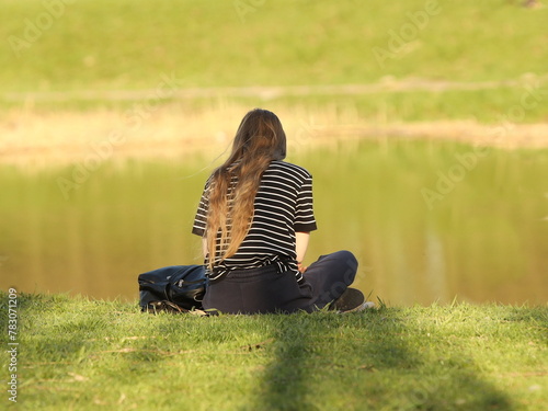 A young girl meditates on the river bank sitting on green grass. Peace of mind and emotional balance. Relaxing alone in nature. Achieving Mental Health