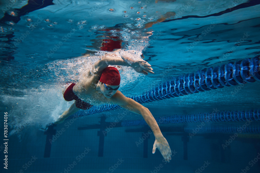 Freestyle stroke. Focused young man, swimmer in motion in swimming pool, training. Athleticism and competitive spirit. Concept of professional sport, health, endurance, strength, active lifestyle
