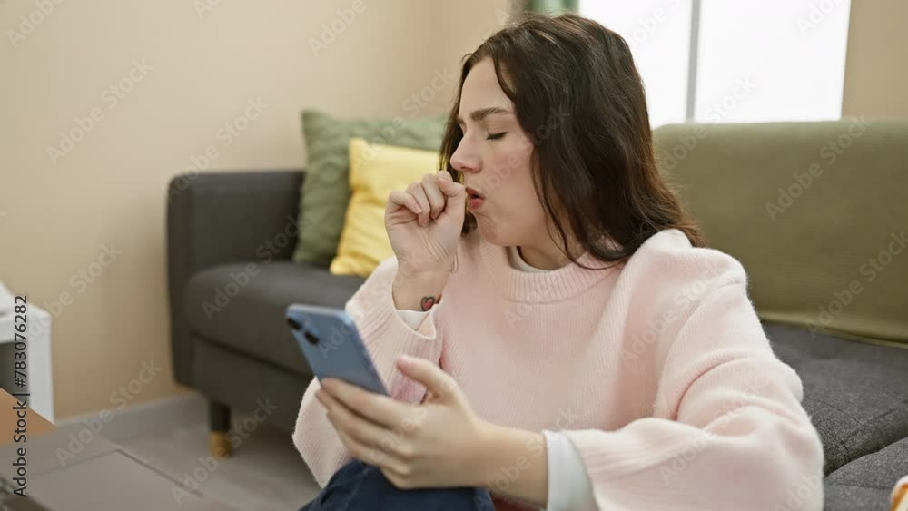 A young woman examines medication while using her smartphone in a cozy living room, feeling unwell A young woman examines medication while using her smartphone in a cozy living room, feeling unwell