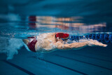 Muscular young man, swimmer in motion, preparing for competition, training in swimming pool indoors. Speed and technique. Concept of professional sport, health, endurance, strength, active lifestyle