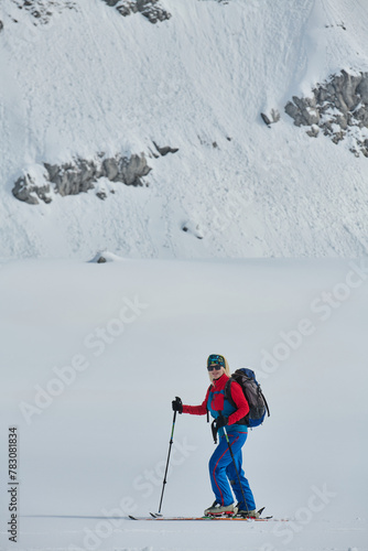 A female skier stands at the snowy summit of a mountain, equipped with professional gear and skis, poised for an exhilarating descent.