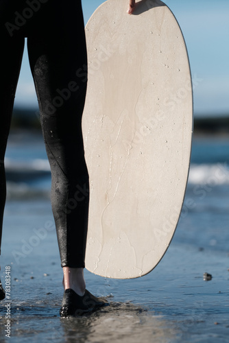 Junge im Neoprenanzug mit Skimboard in der Hand am Strand im Wasser am Meer auf Sardinien