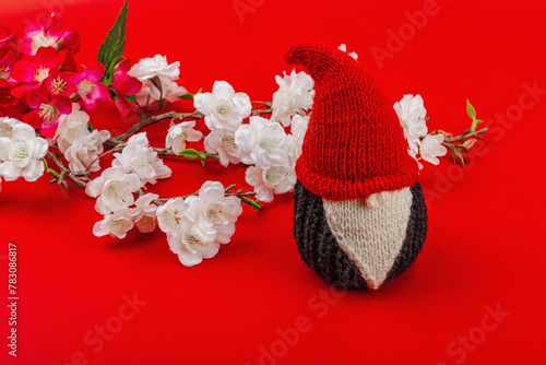 Minimalist spring greeting card with knitted gnome and blooming cherry branches