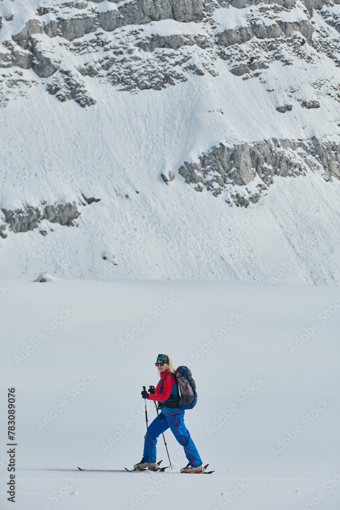 A female skier stands at the snowy summit of a mountain, equipped with professional gear and skis, poised for an exhilarating descent.