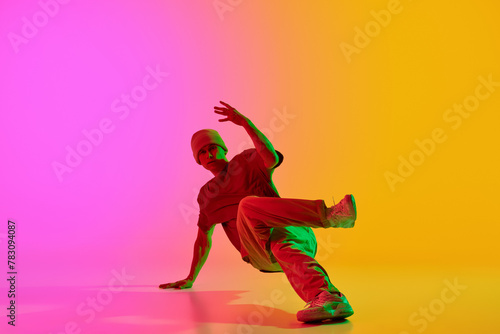 Young athlete man, dressed urban style outfit dancing in motion in neon light against gradient pink-yellow background. Concept of hobby, sport, creativity, fashion and style, action. Ad