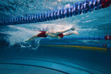 Beauty of athleticism in action. Dynamic image of young man, athlete in motion, swimming in s pool indoors, training. Concept of professional sport, health, endurance, strength, active lifestyle