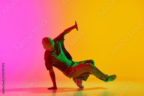 Talented dancer dressed streetwear performing freestyle moves in motion in neon light against gradient pink-yellow background. Concept of art, hobby, sport, creativity, fashion and style, action. Ad