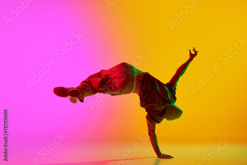 Photography Dynamic photo of young, talented man dancing freestyle moves in neon light against gradient pink-yellow background