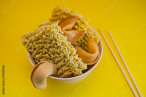 A dried noodles, fortune cookies and chopsticks in a bowl on yellow background.