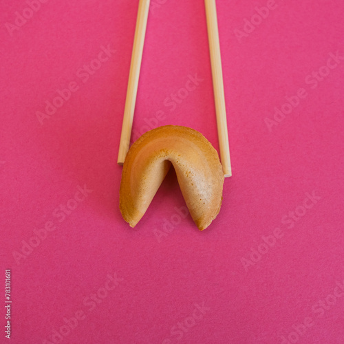 Chopsticks hold a fortune cookie on bright pink background. Flat lay, top view. Minimalism