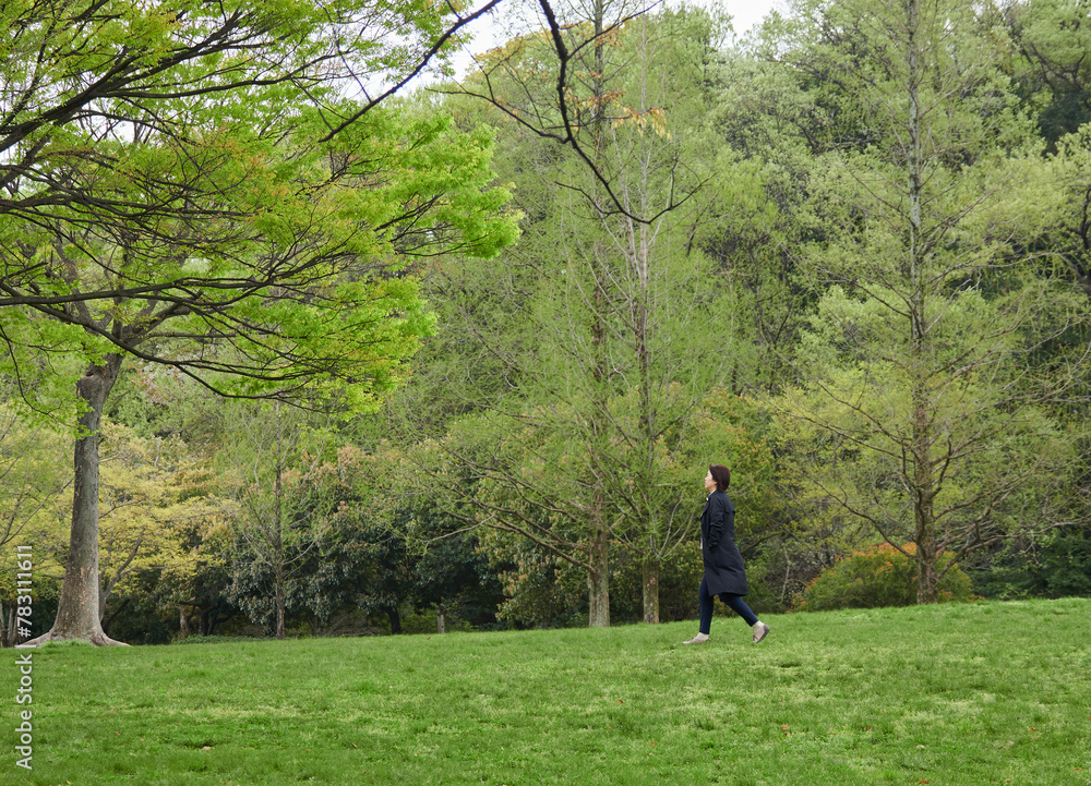 春の新緑の公園で散歩する一人の女性の様子