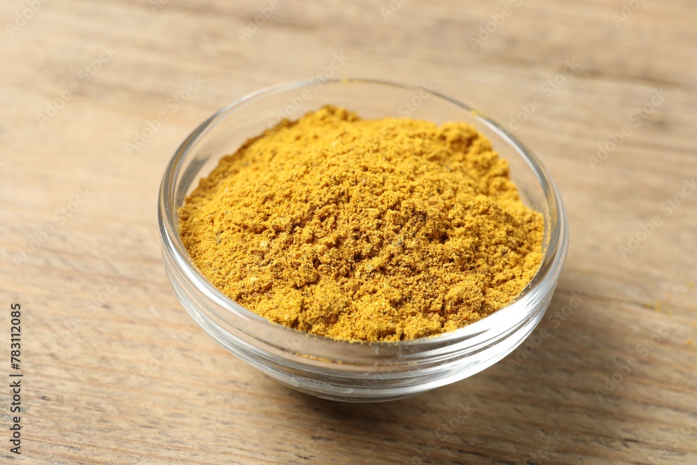 Curry powder in bowl on wooden table, closeup Curry powder in bowl on wooden table, closeup