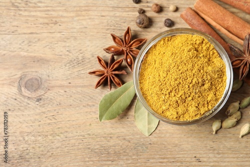 Curry powder in bowl and other spices on wooden table, flat lay. Space for text