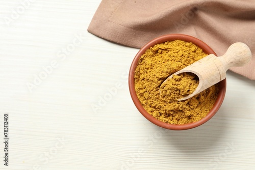 Foto Curry powder in bowl and scoop on white wooden table, top view