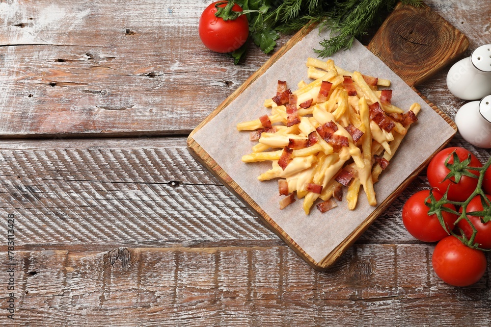 Delicious French fries with bacon, cheese sauce, tomatoes and herbs on wooden table, flat lay. Space for text Delicious French fries with bacon, cheese sauce, tomatoes and herbs on wooden table, flat lay. Space for text