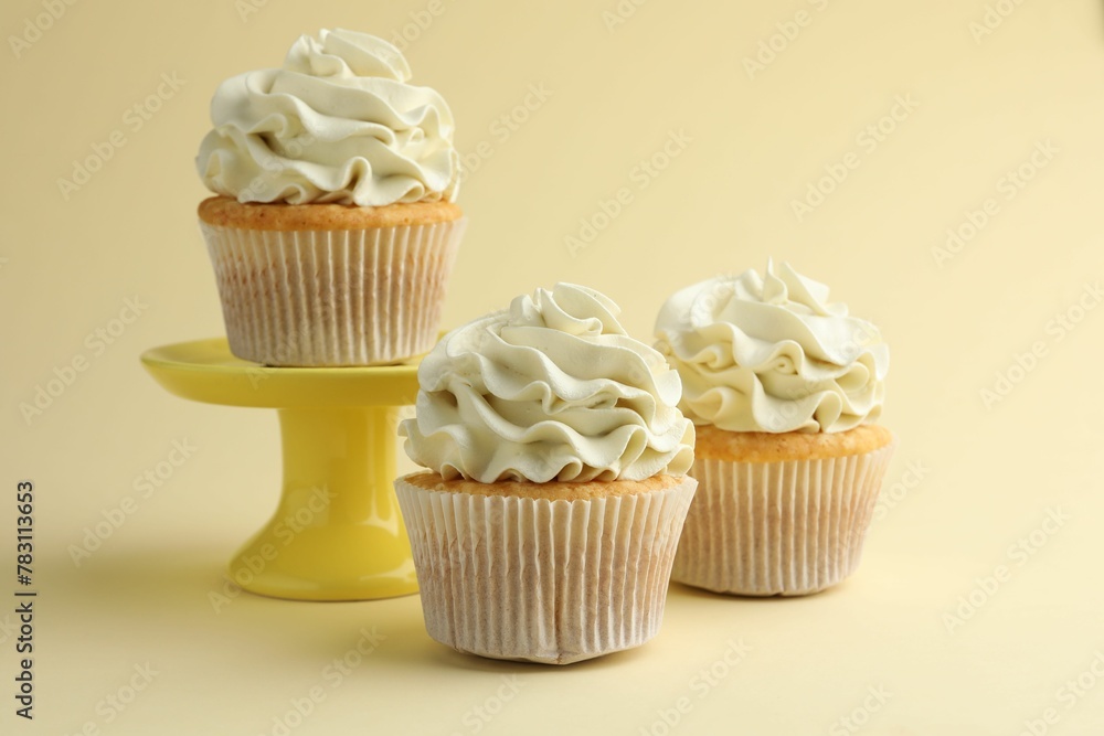 Tasty vanilla cupcakes with cream on pale yellow background Tasty vanilla cupcakes with cream on pale yellow background