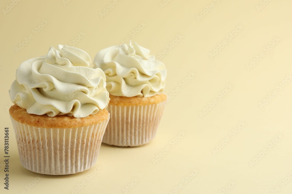 Tasty vanilla cupcakes with cream on pale yellow background, space for text Tasty vanilla cupcakes with cream on pale yellow background, space for text