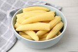 Tasty fresh yellow baby corns in bowl on white wooden table
