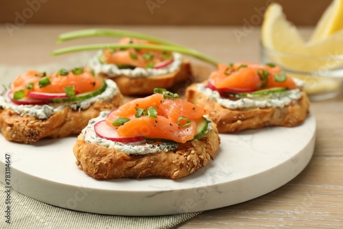 Tasty canapes with salmon, cucumber, radish and cream cheese on wooden table, closeup