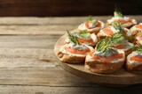 Tasty canapes with salmon, cucumber, cream cheese and dill on wooden stand, closeup. Space for text
