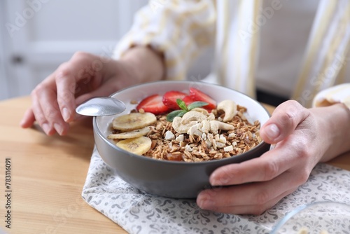 Woman eating tasty granola with banana, cashew and strawberries at wooden table indoors, closeup