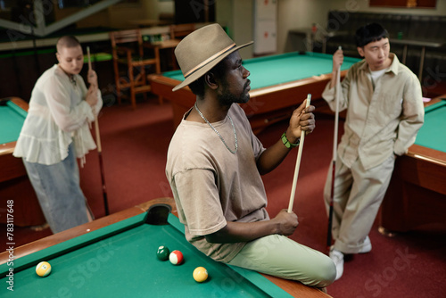 Portrait of African American adult man wearing hat with multiethnic group of people in pool club