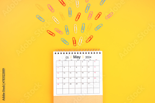 May 2024 desk calendar and colorful metal paperclips on yellow background. © gamjai