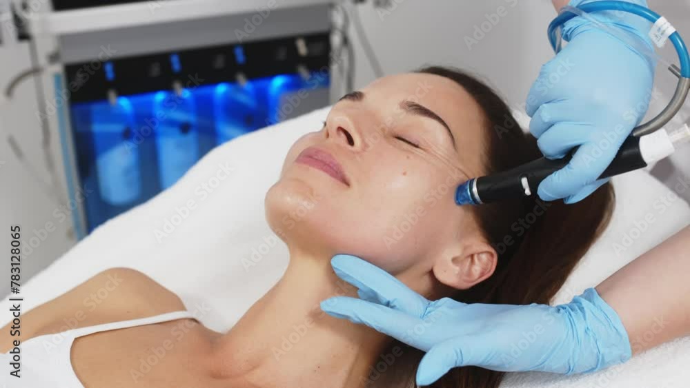 Concept of skin care, rejuvenation and cosmetology. Close-up of a cosmetologist's hands polishing and cleansing the facial skin of a middle-aged woman using a vacuum machine. Concept of skin care, rejuvenation and cosmetology. Close-up of a cosmetologist's hands polishing and cleansing the facial skin of a middle-aged woman using a vacuum machine.