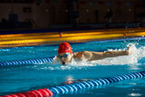Young muscular man showing competitive spirit, swimmer in cap and goggles training, swimming in pool, preparing for competition. Concept of professional sport, health, endurance, active lifestyle
