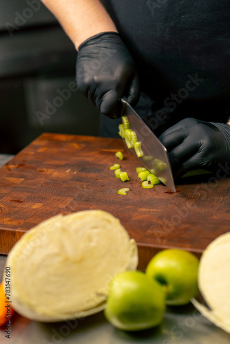 close-up in a professional kitchen wearing black gloves cuts celery on wooden board