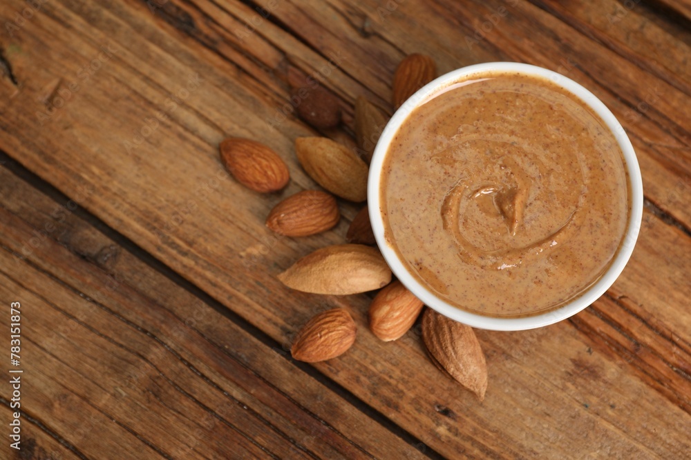 Delicious nut butter in bowl and almonds on wooden table, top view. Space for text Delicious nut butter in bowl and almonds on wooden table, top view. Space for text
