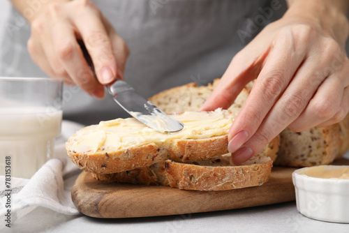 Woman spreading tasty butter onto bread at table, closeup