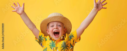 A young boy dressed in summer attire, wearing yellow shirt and straw hat with closed eyes is making peace sign while laughing out loud against vibrant yellow background. photo