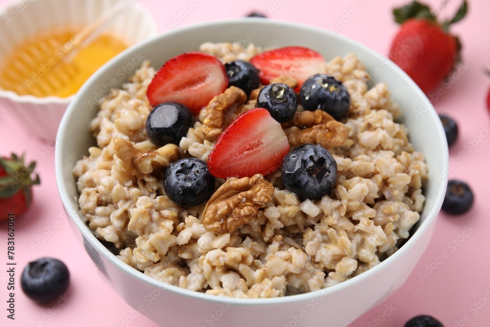 Tasty oatmeal with strawberries, blueberries and walnuts in bowl surrounded by fresh berries on pink background, closeup Tasty oatmeal with strawberries, blueberries and walnuts in bowl surrounded by fresh berries on pink background, closeup