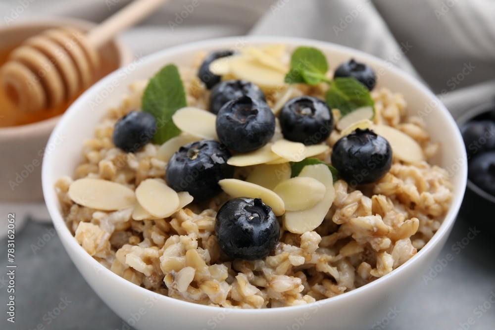 Tasty oatmeal with blueberries, mint and almond petals in bowl on grey table, closeup Tasty oatmeal with blueberries, mint and almond petals in bowl on grey table, closeup