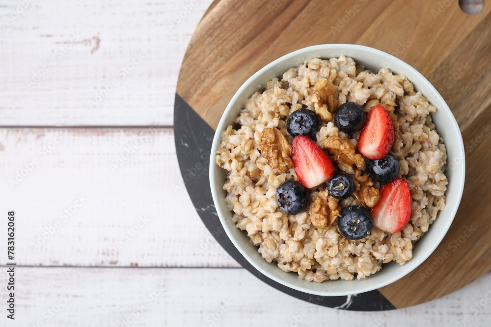 Tasty oatmeal with strawberries, blueberries and walnuts in bowl on white wooden table, top view Tasty oatmeal with strawberries, blueberries and walnuts in bowl on white wooden table, top view