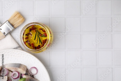 Tasty fish marinade in jar and herring on light tiled table, flat lay. Space for text