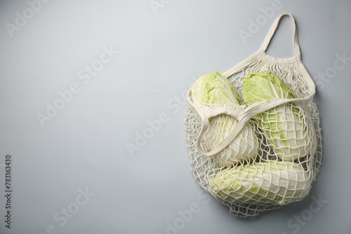Fresh Chinese cabbages in string bag on light background, top view. Space for text